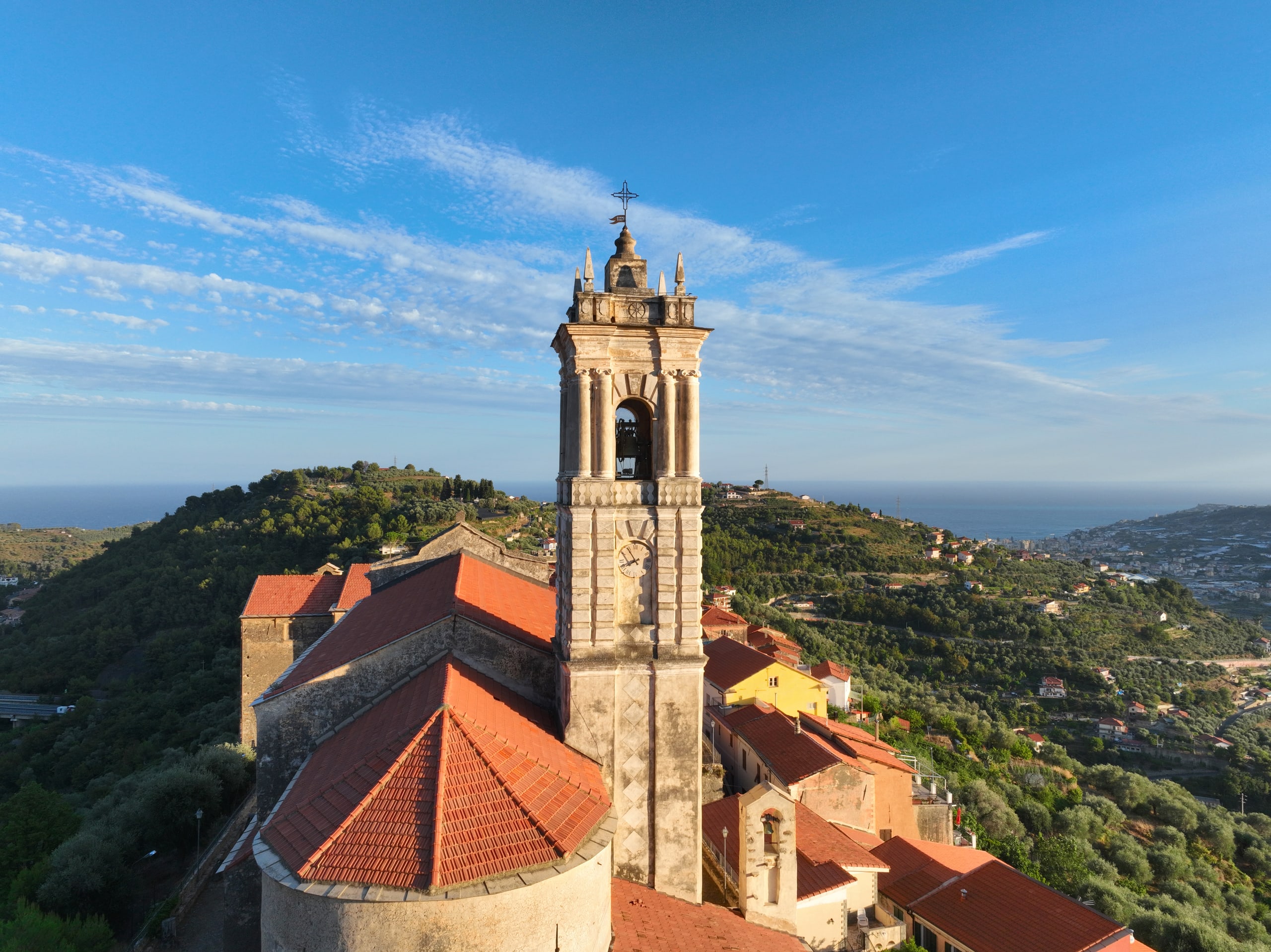 Aerial view of a hilltop church bell tower above a coastal town, sea on the horizon