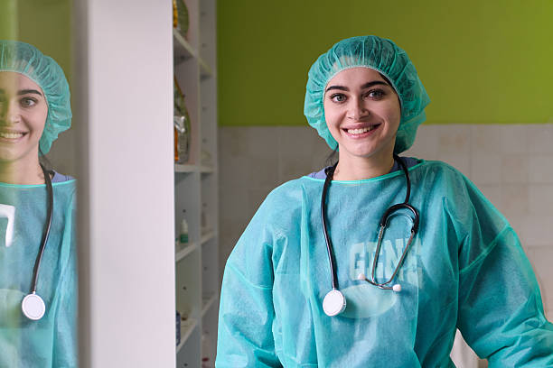 A smiling young clinician in a green gown and cap with a stethoscope