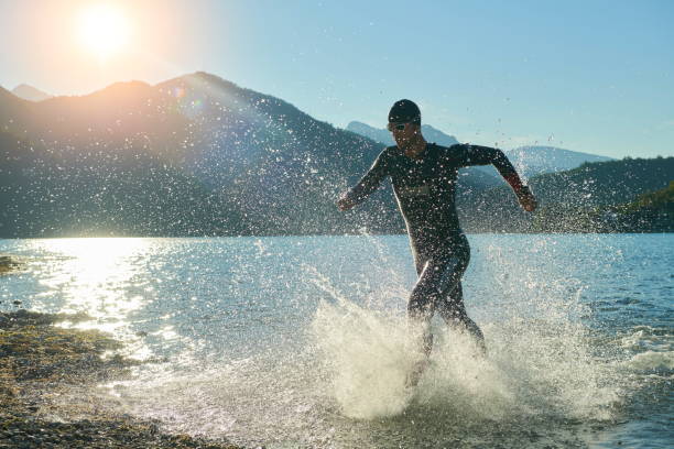 A triathlete in a wetsuit running out of a lake, water splashing