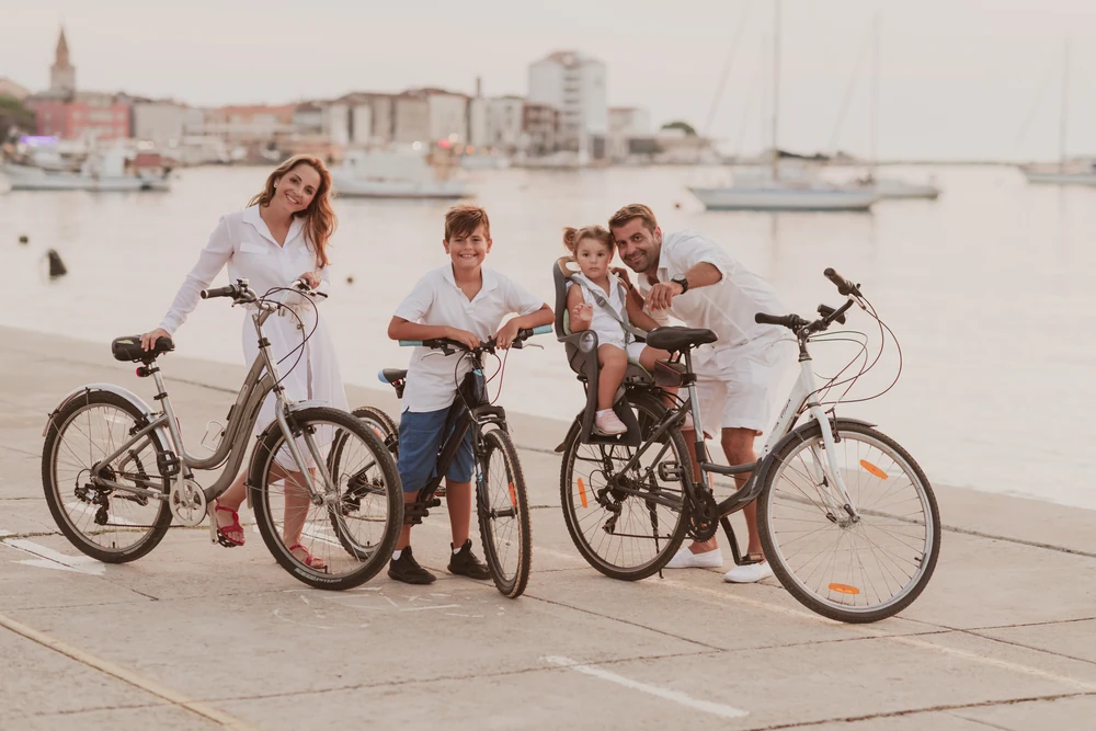 A family of four with bicycles on a waterfront promenade