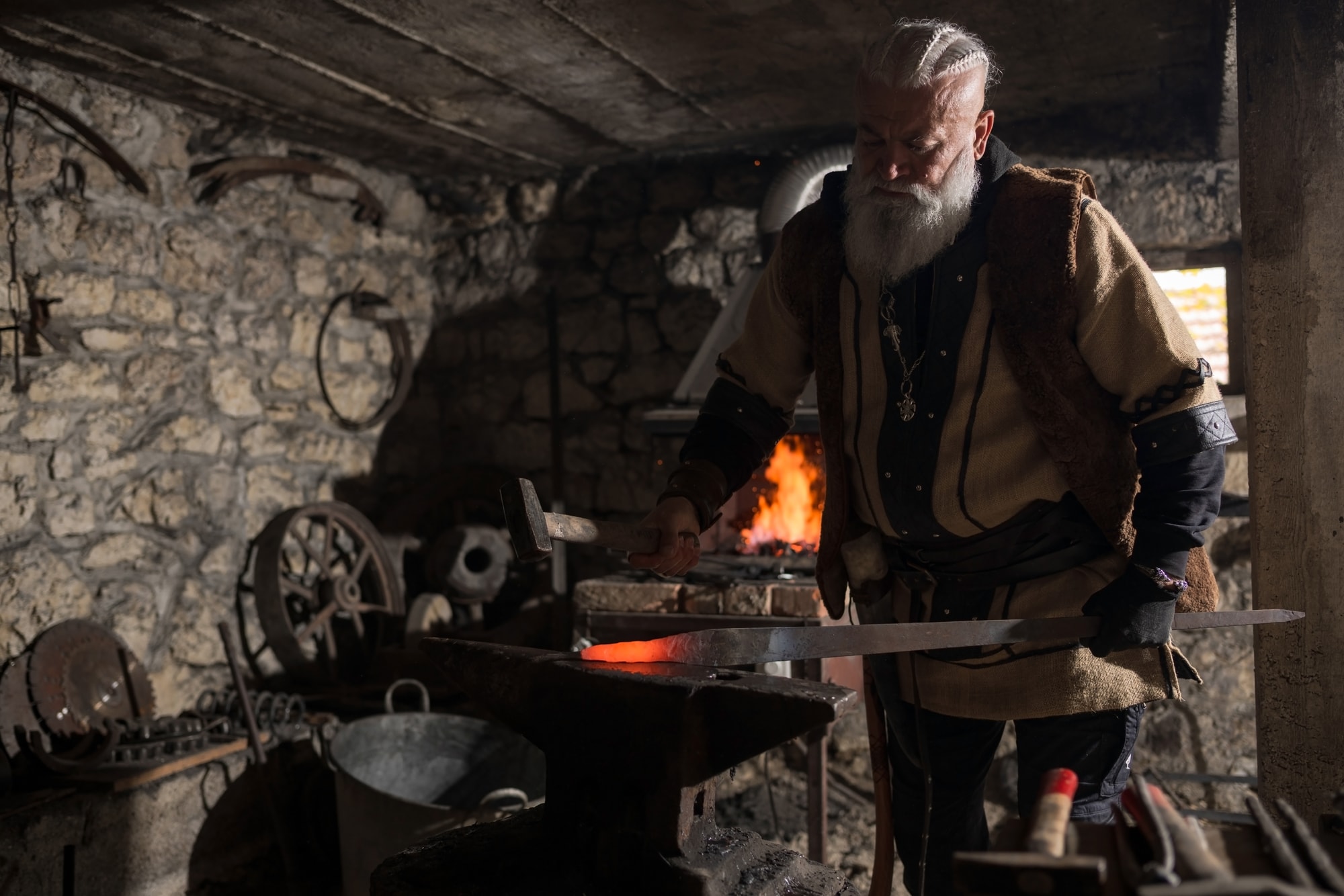 A white-bearded blacksmith working at a glowing forge in a stone workshop