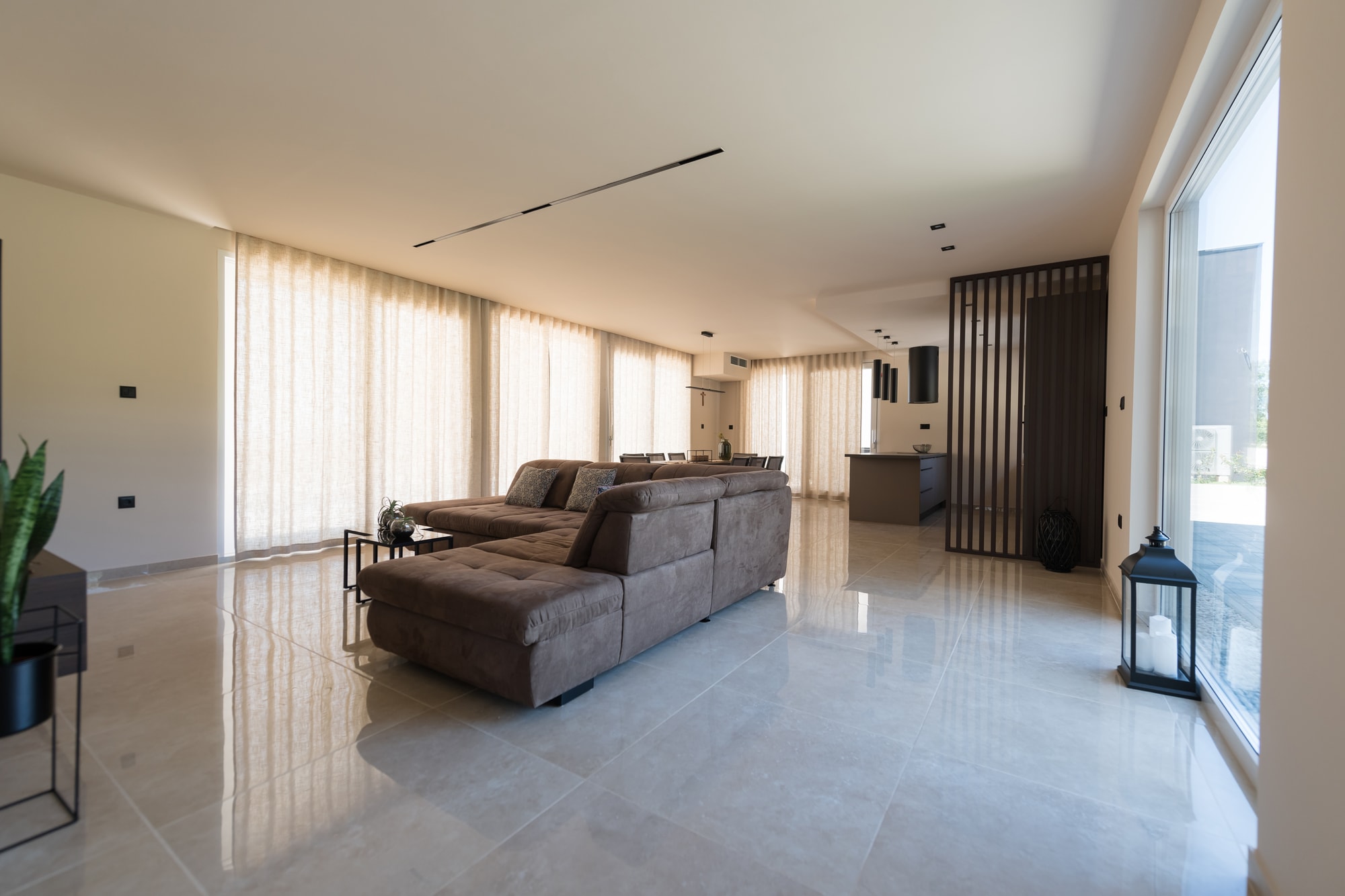 A modern open-plan living room with floor-to-ceiling windows and a polished stone floor