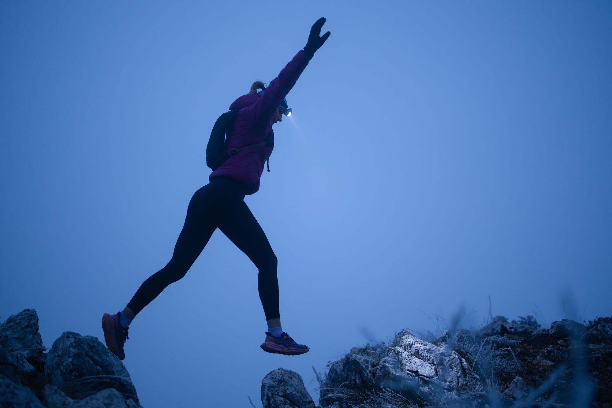 A runner with a head torch leaping between rocks at dusk