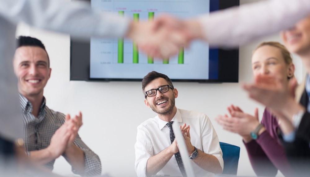 Colleagues applauding in a meeting room as two people shake hands